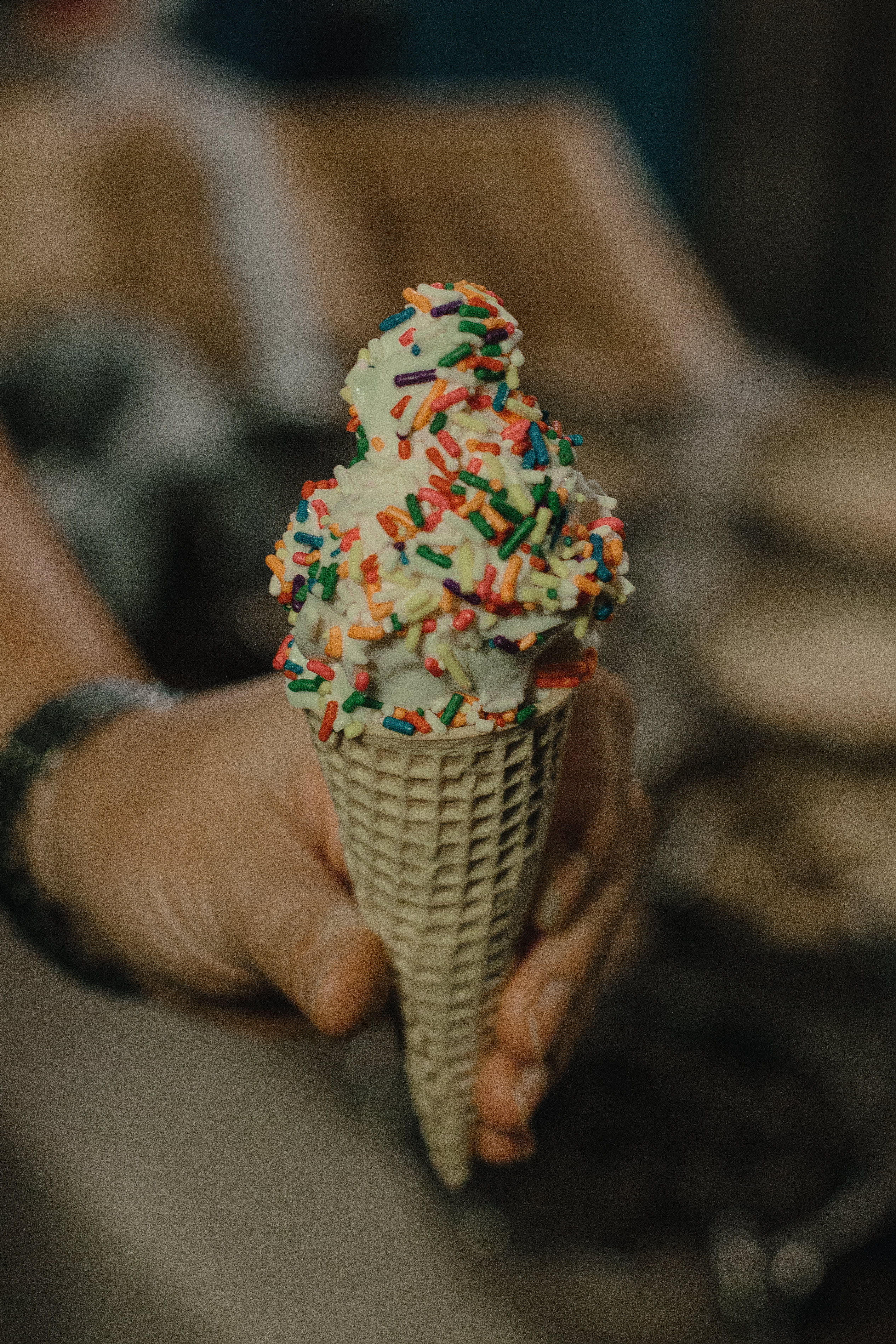 a closeup image of a hand holding a soft service ice cream cone with sprinkles