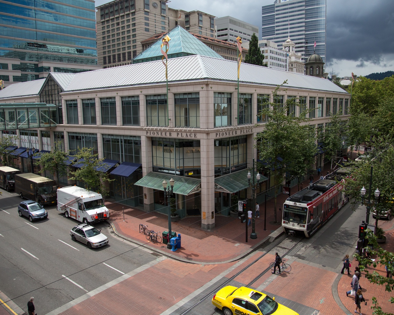 the exterior of a large urban shopping mall with vehicles and a light rail train out front