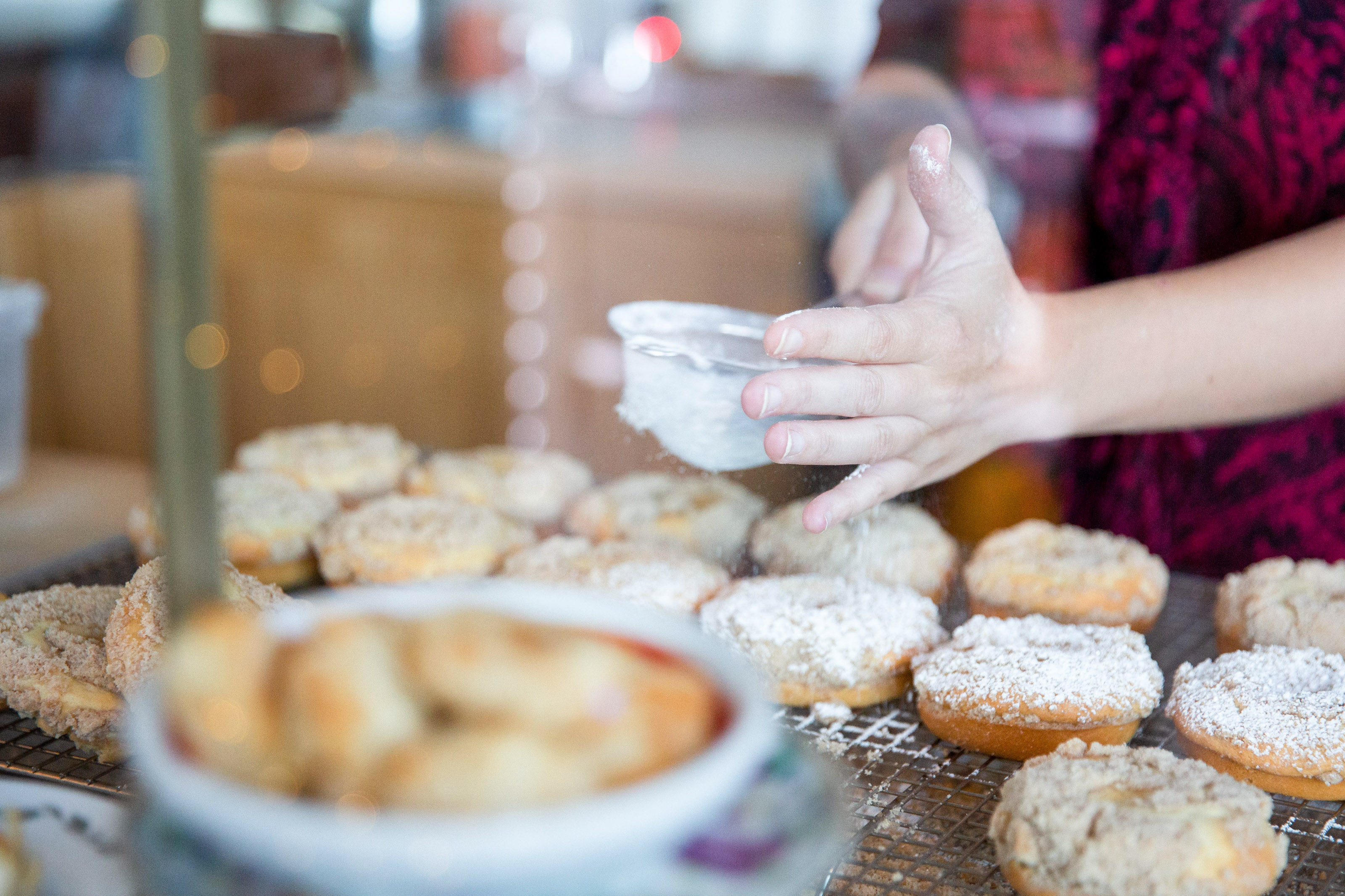 A person sprinkles powdered sugar over pastries