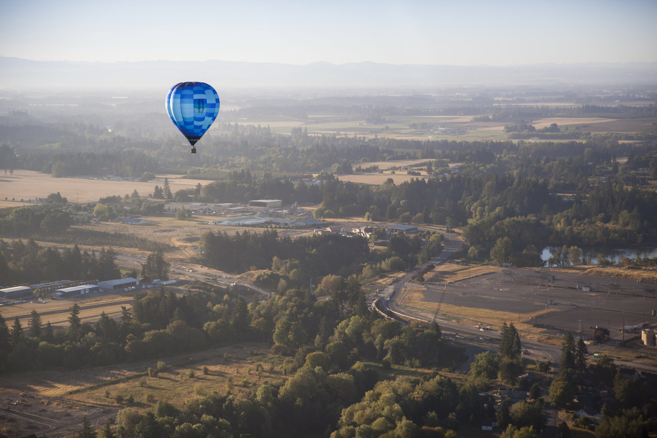 A hot air balloon floats above a wooded valley.