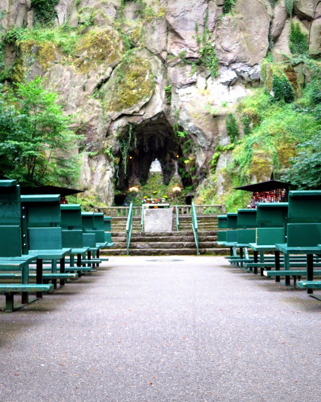 rows of benches face a rock wall and tunnel surrounded by moss, trees