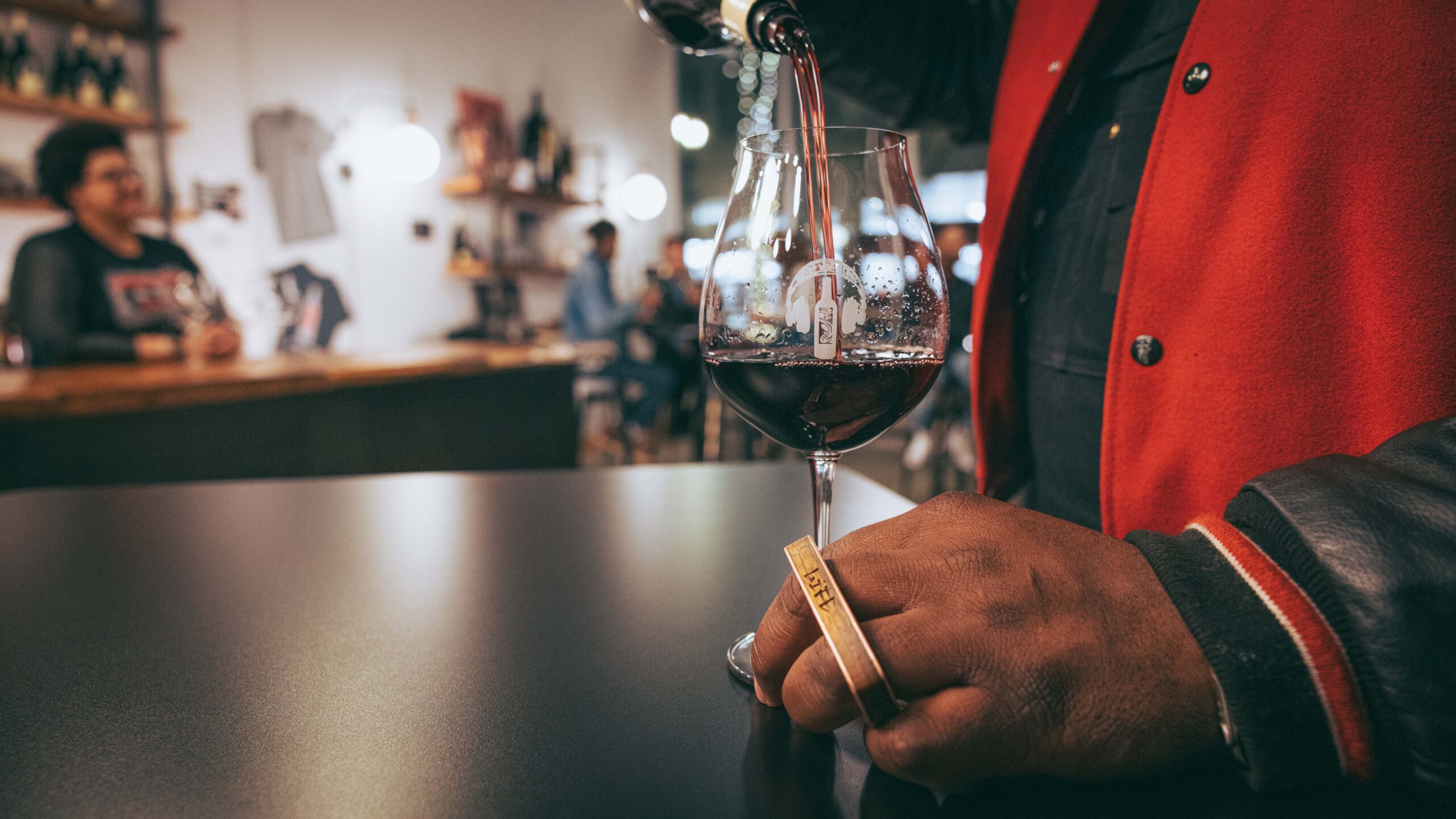 man with a gold finger ring holds a wine glass stem and pours a drink