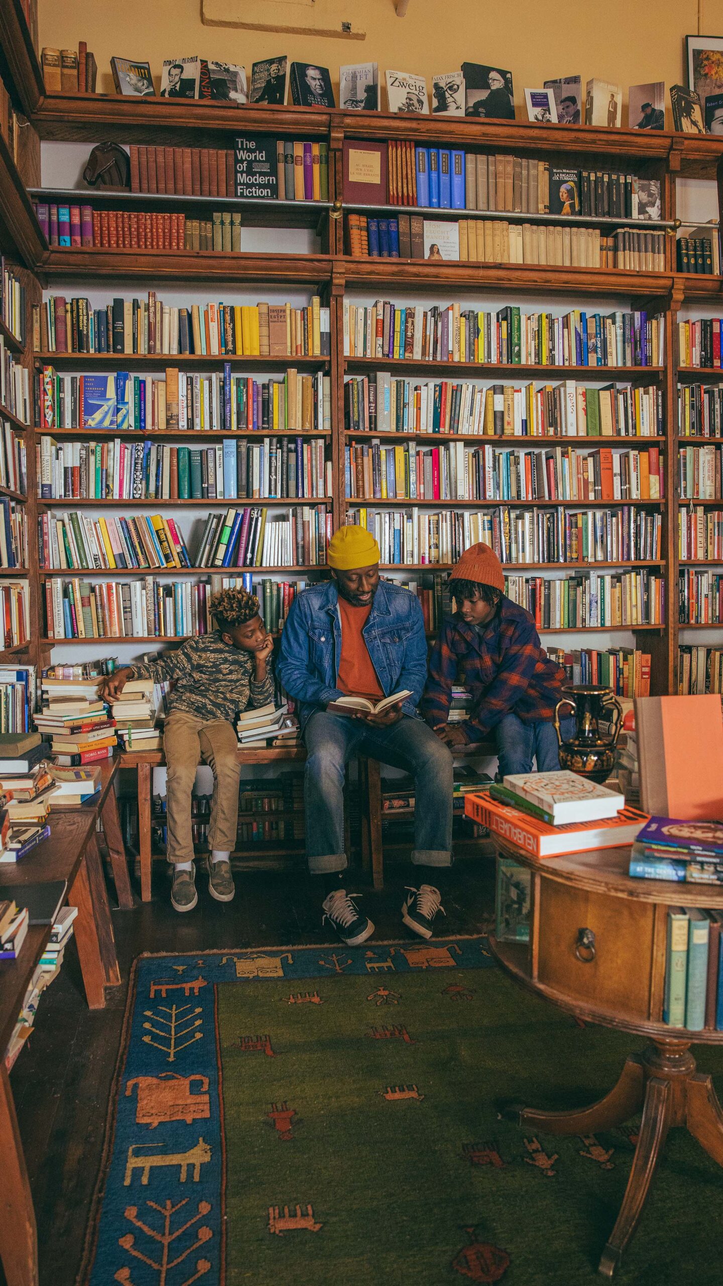 Three people sit and read a book at Mother Foucault\'s bookstore in front of a wall of books.