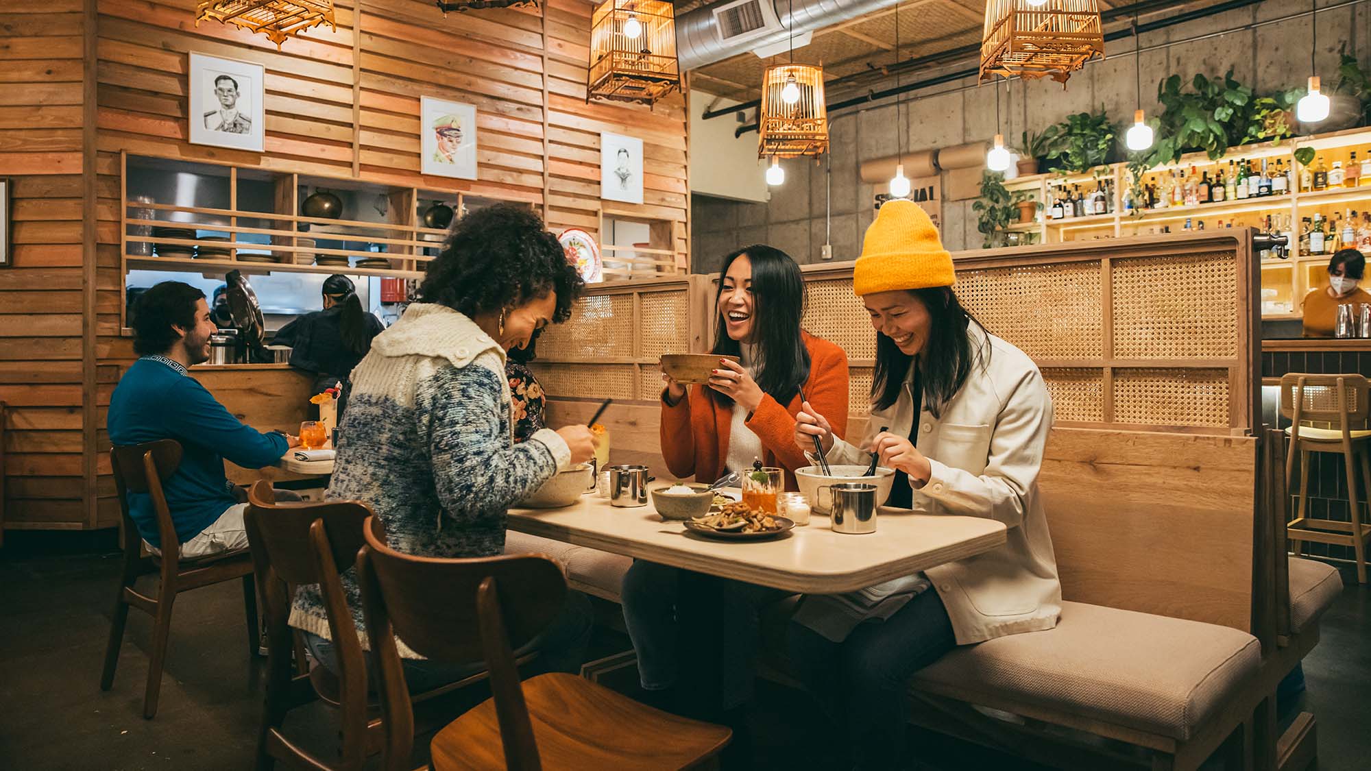 friends enjoy large bowls of Thai fare in a warmly lit restaurant