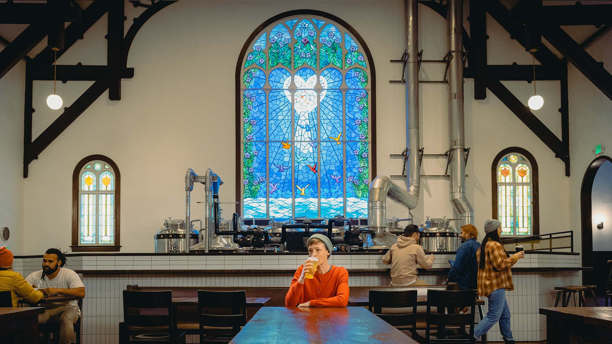 a person sips a beer in front of a stained glass window
