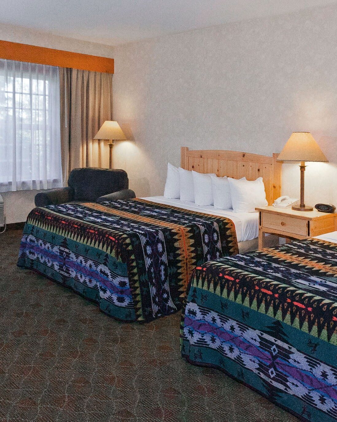 two queen sized beds covered with colorful blankets with geometric patterns in a hotel room