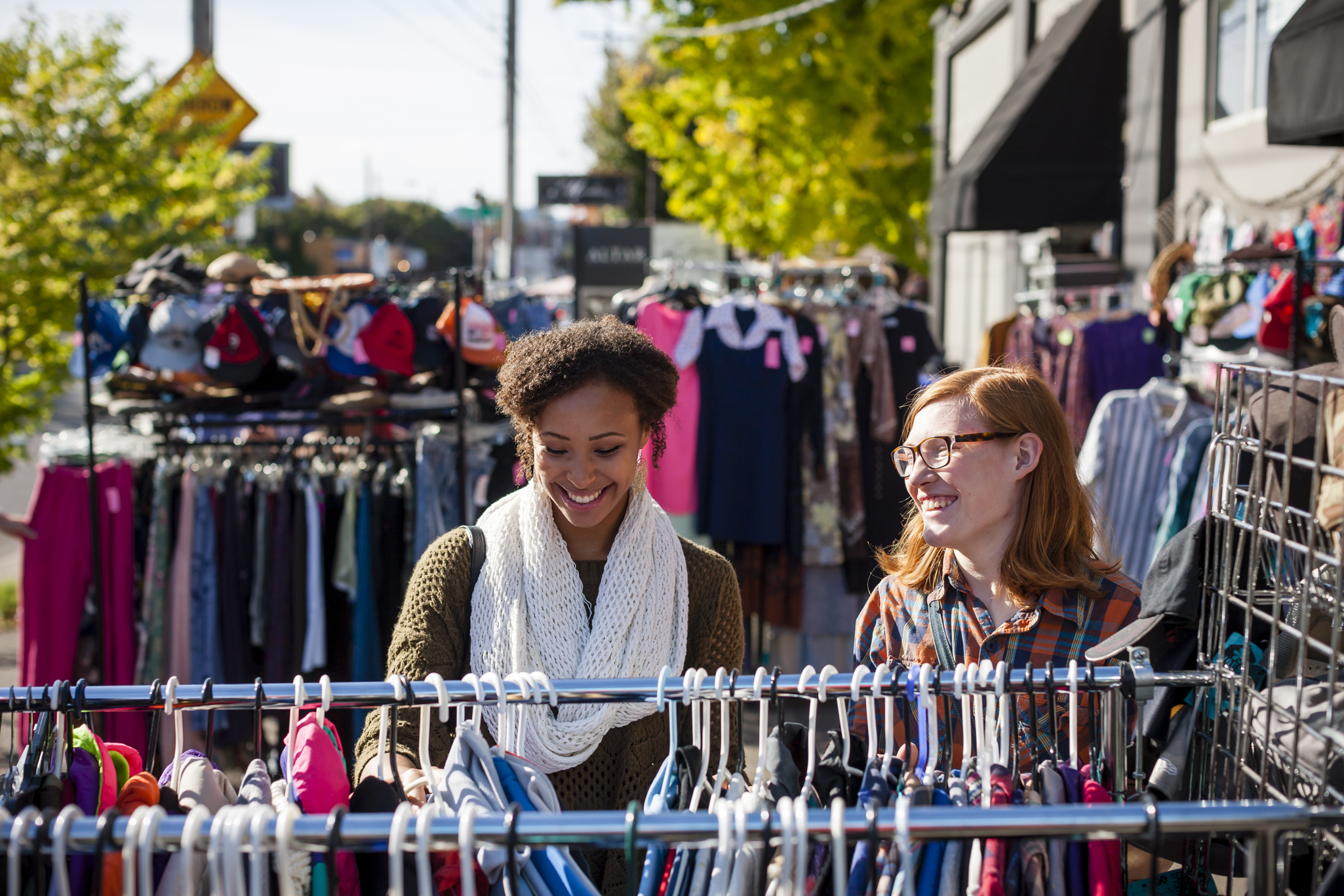 two people look through outdoor racks of clothing on a sunny day