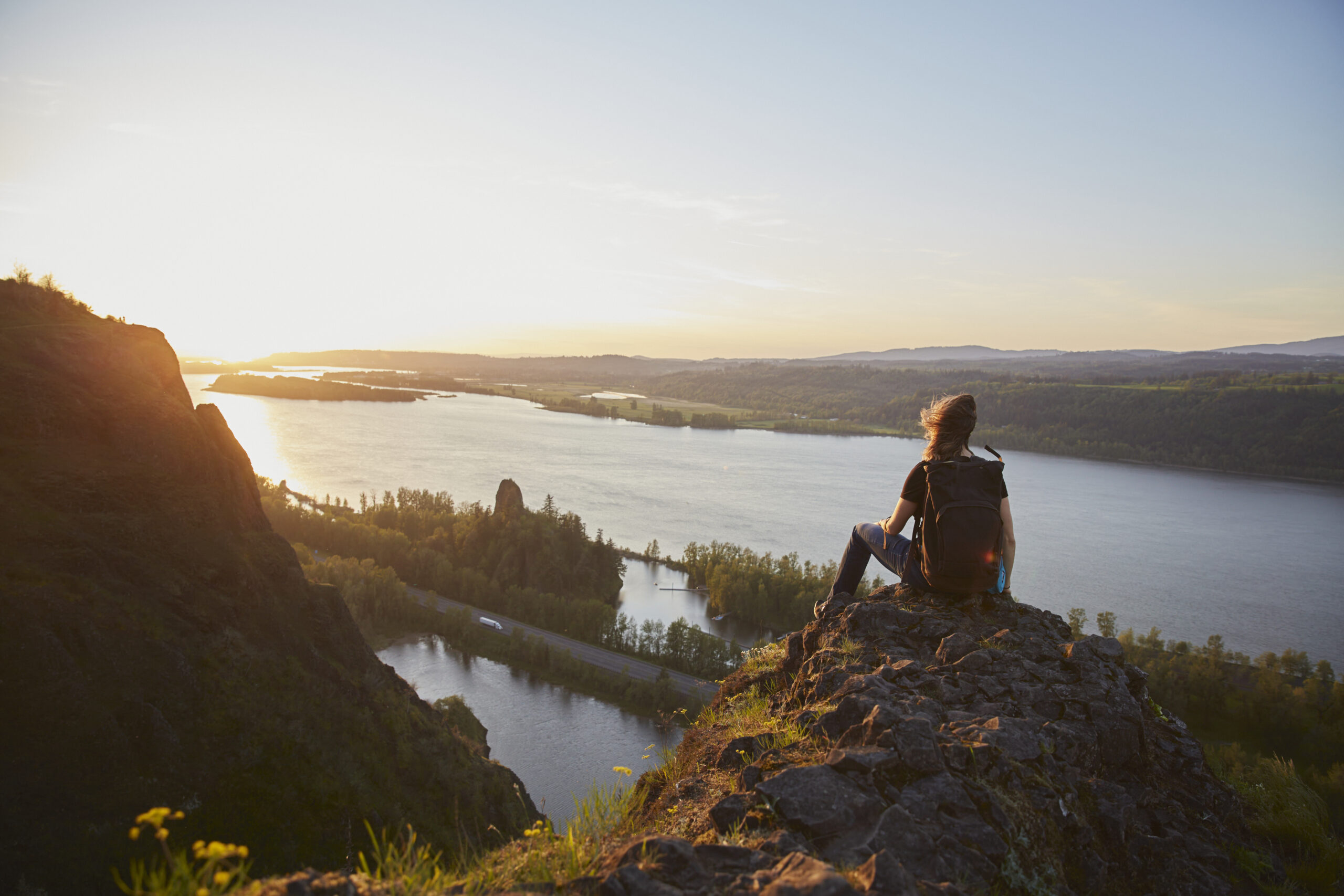 person sits on top of a rock overlooking the Columbia River as the sun sets