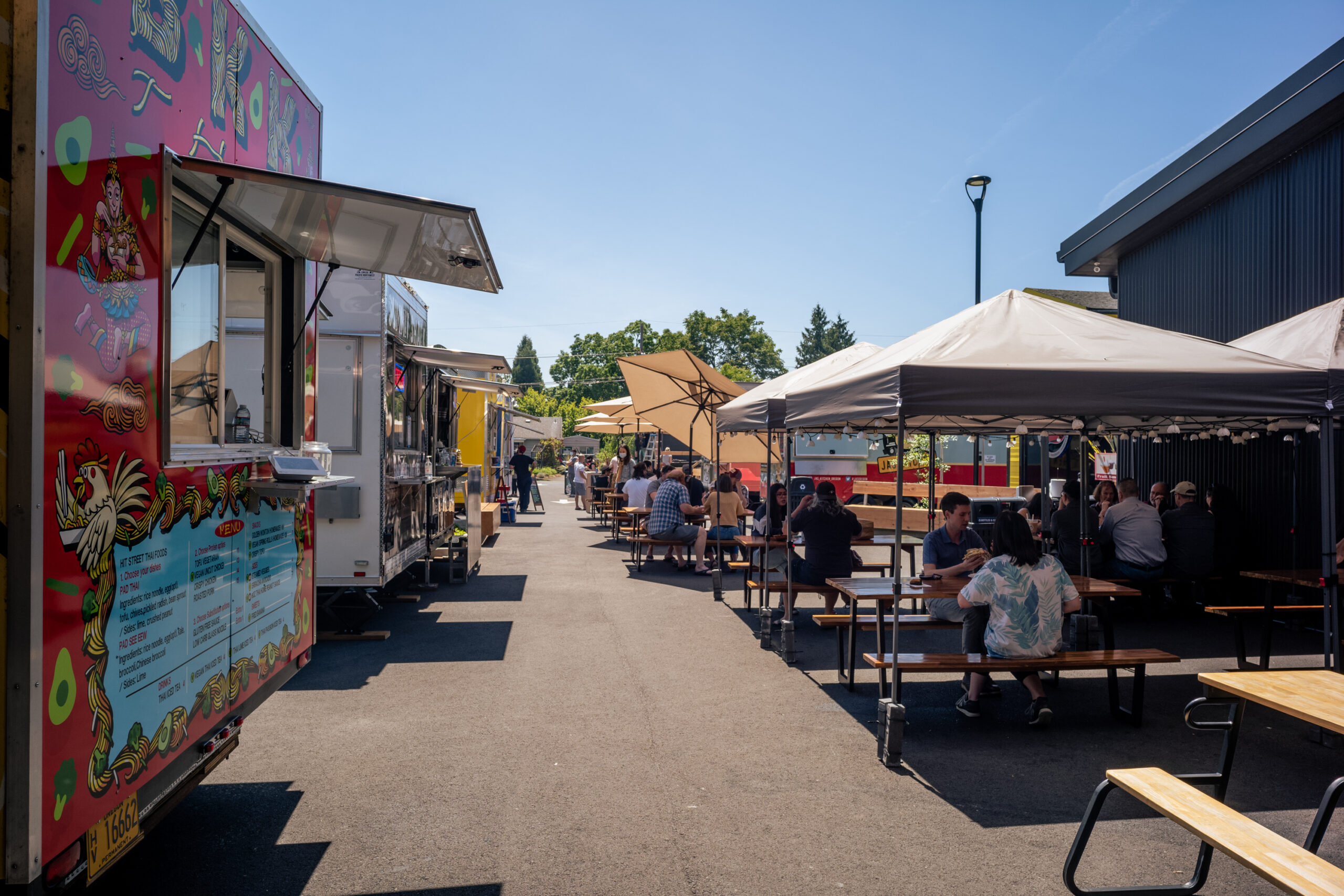 a row of food carts and diners enjoying covered outdoor seating on a sunny day