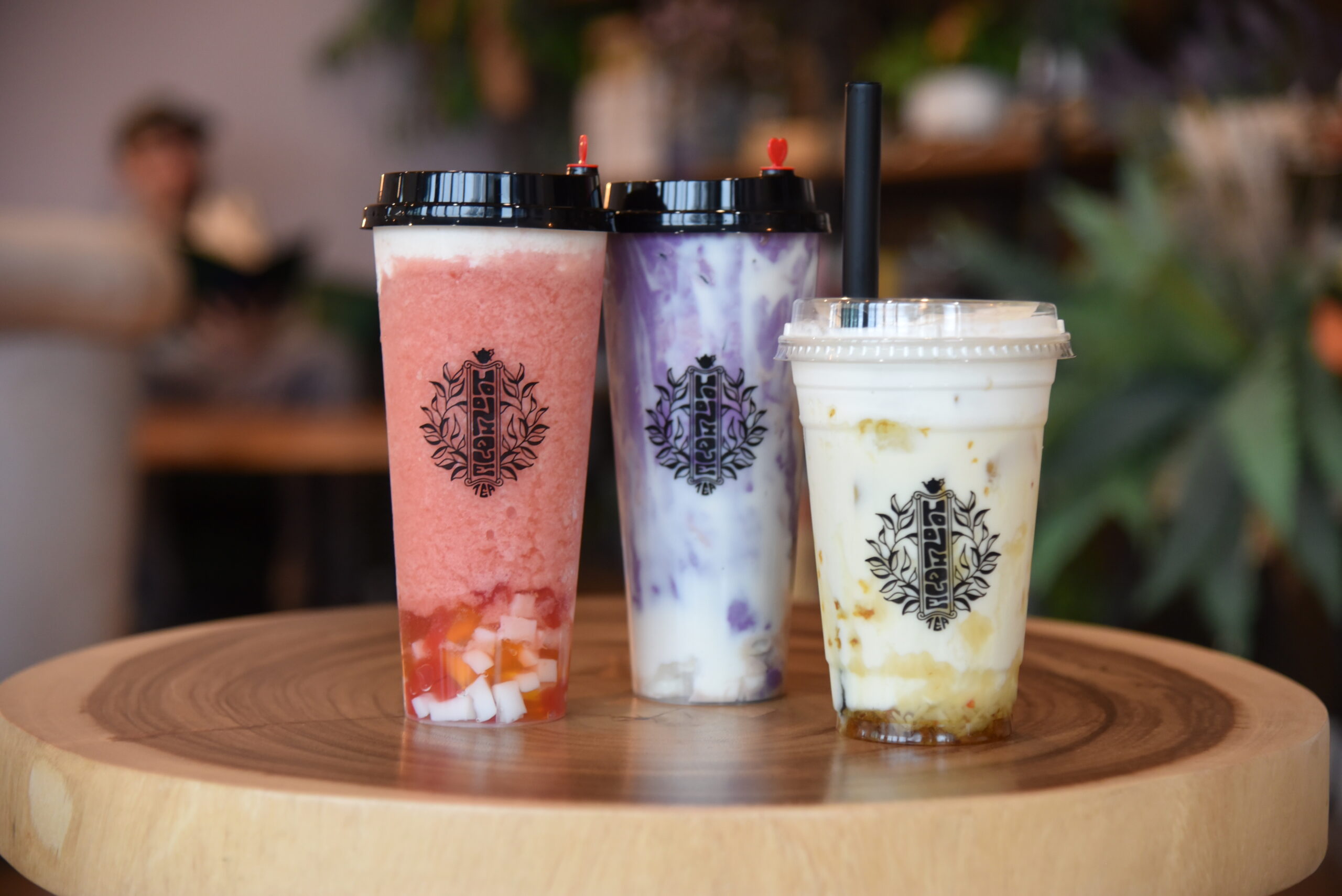 Three cups of flavored boba tea rest on small wooden table.