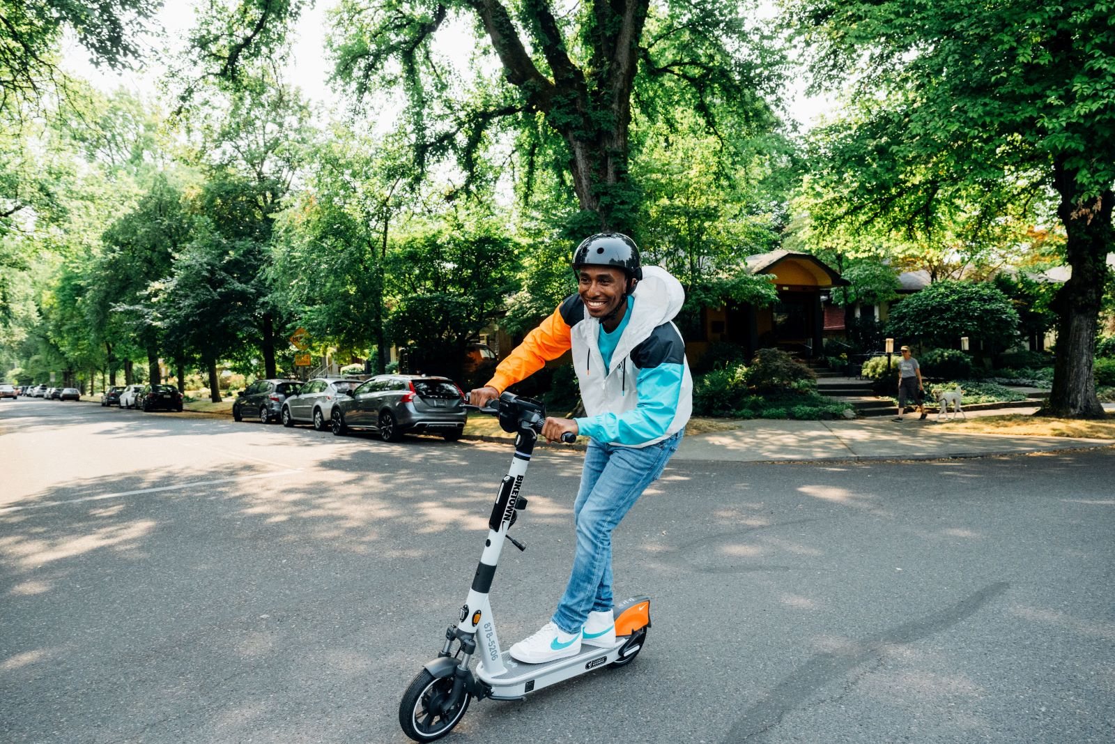 a smiling man wearing a helmet rides a Biketown scooter on a leafy city street