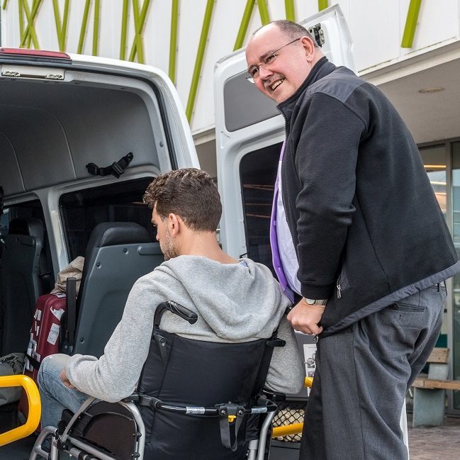 One man helps another man in a wheelchair into a van