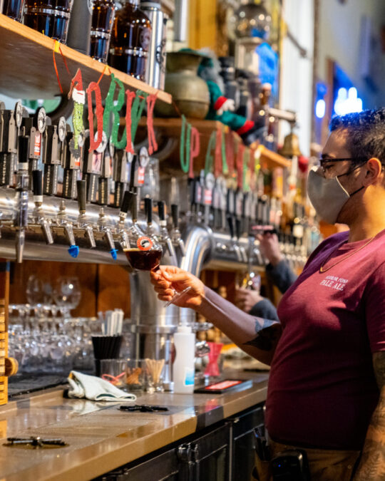a person pours a dark draft beer from a long line of taps